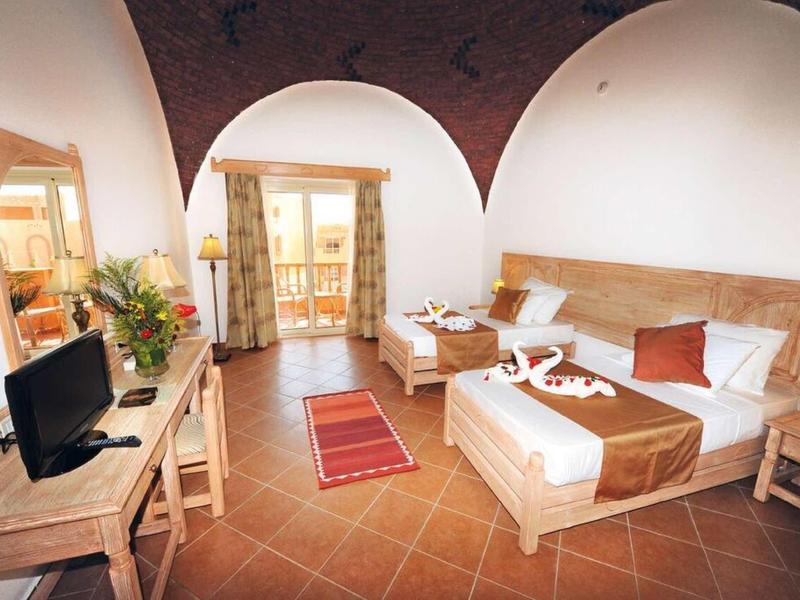 Geräumiges Schlafzimmer mit Balkon, Holzmöbeln, Fliesenboden und warmen Erdtönen.