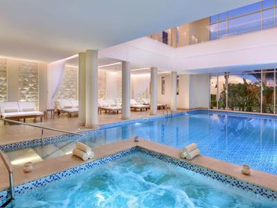 Moderner Wellnessbereich mit Hallenbad und beleuchtetem Whirlpool, stilvolle Sitzbereiche und Glasfenster.