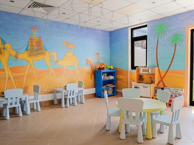 Kinderspielraum mit bunten Tischen, Stühlen und Wandmalerei von Kamelen in Wüstenlandschaft.