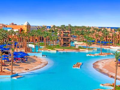 Duży basen hotelowy otoczony palmami i leżakami pod czystym niebieskim niebem.