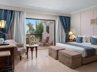 Elegant hotel room with king-size bed, balcony, and sea view by day.