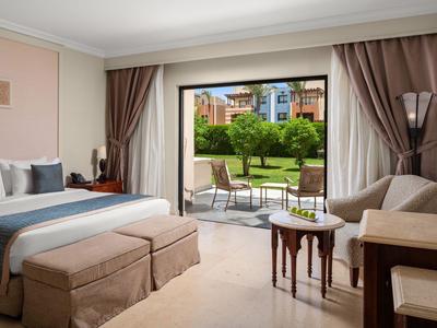 Modern hotel room with double bed, armchairs, and terrace garden view.