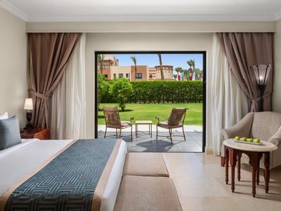 Hotel room with view of terrace and garden featuring chairs and table.