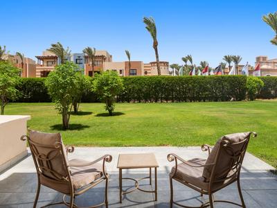 Two chairs and a small table on a terrace overlooking a well-kept garden and palm trees.
