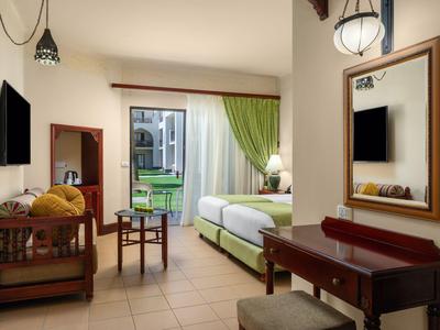 Bright hotel room with bed, seating area, desk, and garden view.