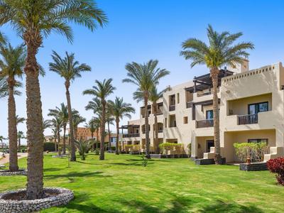 Hotelgebäude mit Balkonen neben einem gepflegten Rasen und Palmen unter klarem Himmel.