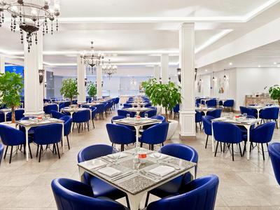 Helles, modernes Restaurant mit blauen Stühlen, weißen Tischen und grünen Pflanzen.