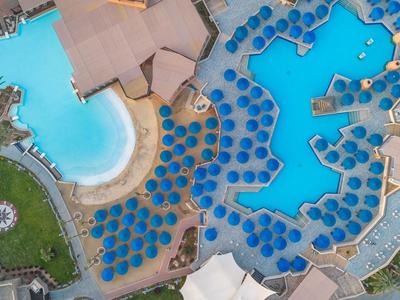 Luftaufnahme eines großen Hotels mit mehreren Pools, Sonnenliegen und Sonnenschirmen.