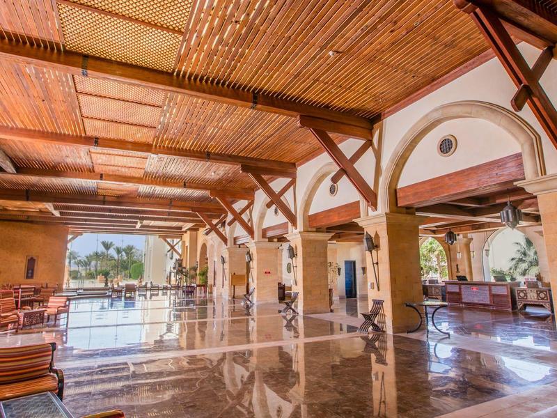 Offene Halle mit Holzdach, Stühlen, Tischen und Blick auf den Pool im Sonnenlicht.