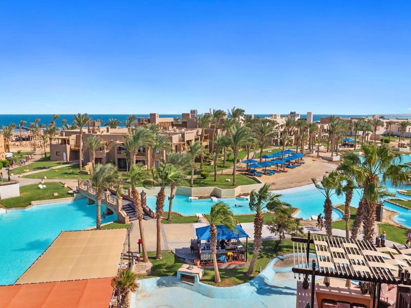 Große Hotelanlage mit mehreren Poolbereichen, Palmen, Liegestühlen und Blick auf das Meer.