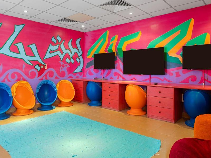 Bunter, moderner Jugendbereich mit bunten Sitzkugeln, Graffiti-Wand und Monitoren.