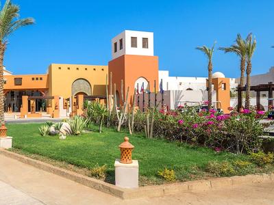 Modern hotelcomplex met mediterrane stijl, palmbomen en goed onderhouden tuin onder een blauwe lucht.