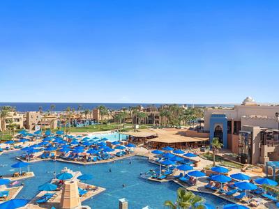 Resort zwembad met blauwe ligbedden en parasols onder heldere hemel bij uitzicht op oceaan.