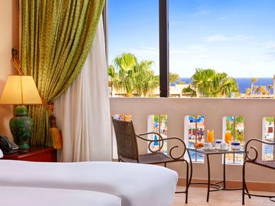 Světý hotelový pokoj s balkonem, výhledem na moře a kovovým nábytkem.