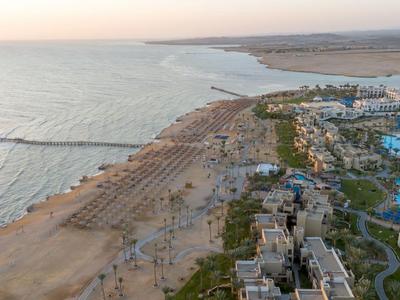 Luftaufnahme eines Strandes mit Liegestühlen und einem Resort mit Pools in der Nähe.