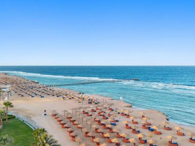 Strand met rijen parasols en ligstoelen bij helderblauwe zee onder een blauwe lucht.