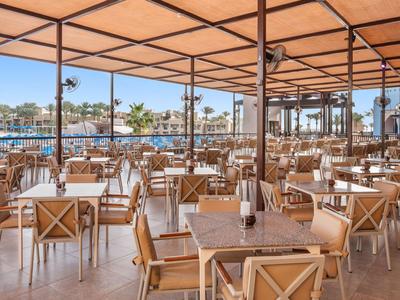 Ruim open restaurant met houten tafels en stoelen onder een luifel met uitzicht op de jachthaven.