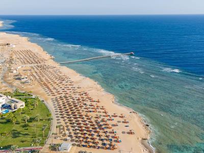 Uitgestrekt zandstrand met rijen parasols en helderblauwe zee.