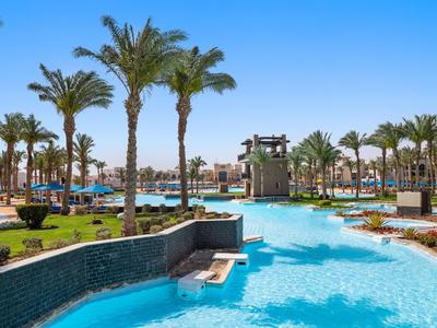 Groot hotelzwembad met palmbomen en ligstoelen onder een heldere blauwe lucht.