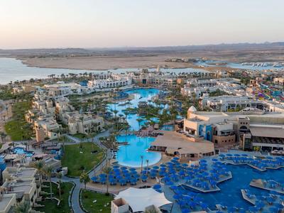 Uitzicht op een groot resort met meerdere zwembaden, parasols en kustlijn op de achtergrond