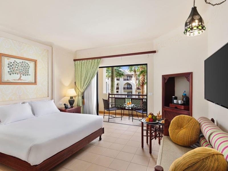 Světle zařízený hotelový pokoj s manželskou postelí, terasou a výhledem na tropickou zahradu.