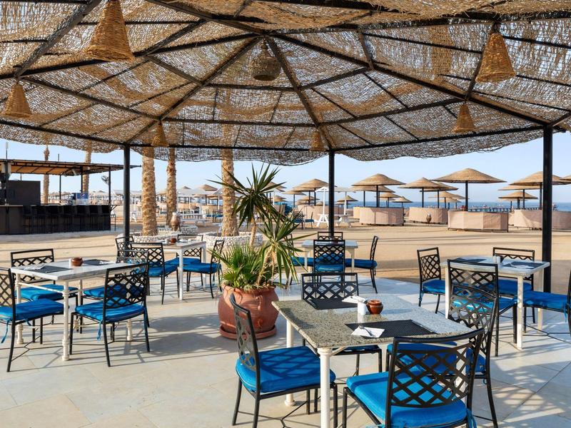 Zastíněná terasa s stolky a židlemi u pláže a slunečníky.