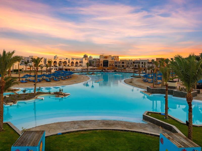 Luxusní hotelový bazén s palmami a barevnou oblohou za soumraku.