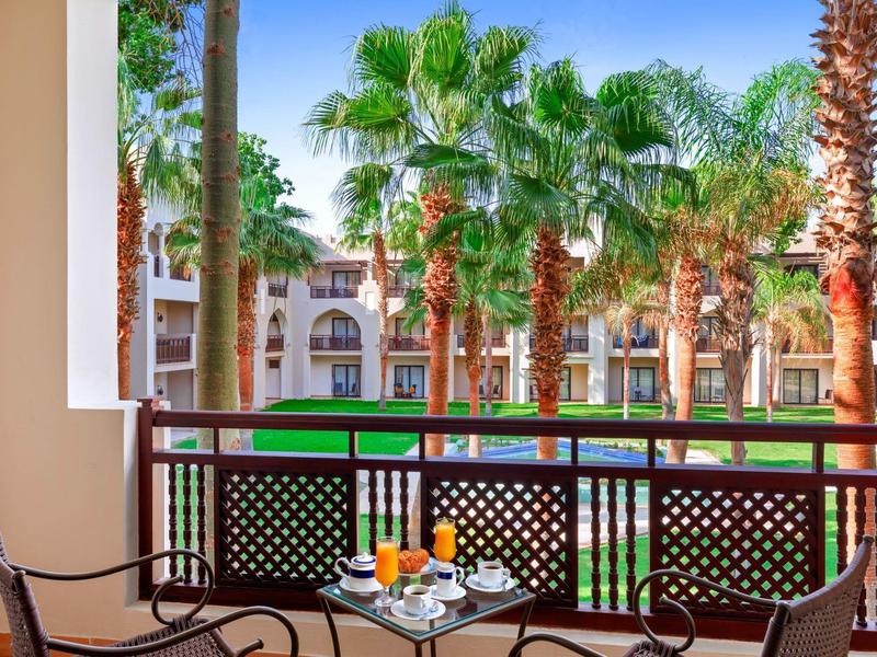 Terasa se stolem a nápoji s pohledem na palmy a hotel v pozadí.