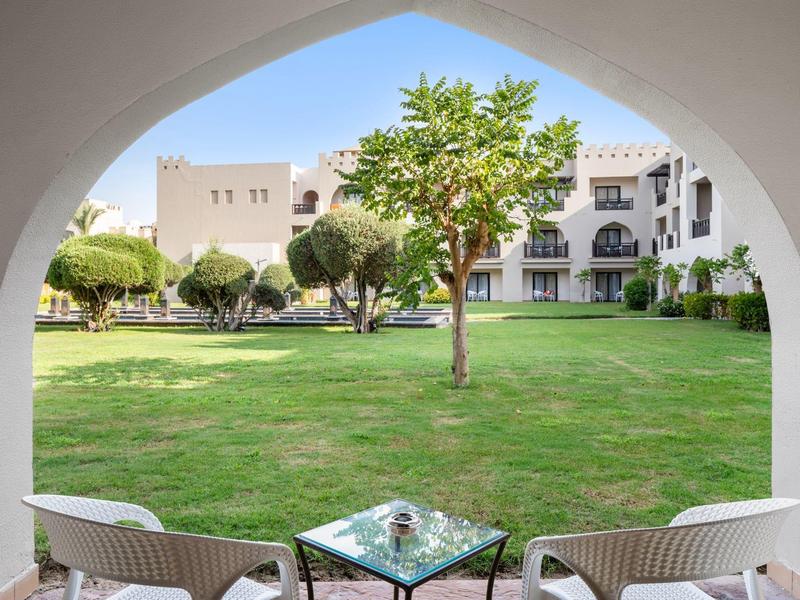 Poklidný výhled na zelenou zahradu se stoly a židlemi pod bílým obloukem.