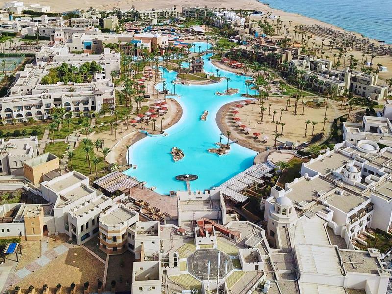 Letecký pohled na hotelový komplex s velkým bazénem a pláží v pozadí.