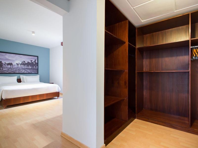 Lichte hotelkamer met groot bed en open houten kast met hangrail.