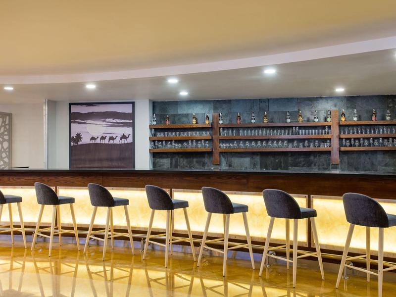 Moderne hotelbar met zeven krukken en een lange houten bar onder warm licht.