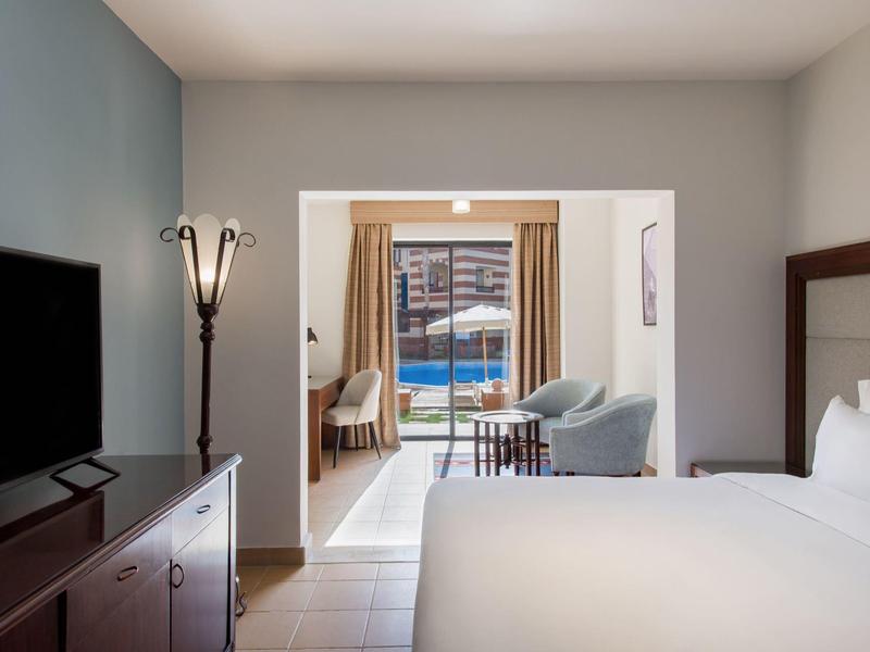 Hotelkamer met tweepersoonsbed en uitzicht op het zwembad door een open deur.