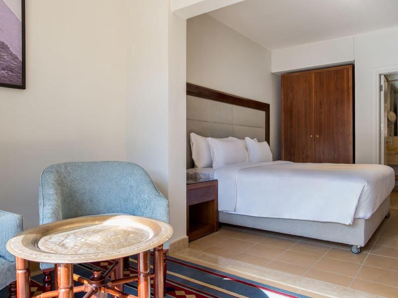 Licht ingericht hotelkamer met tweepersoonsbed, zithoek en houten meubels.