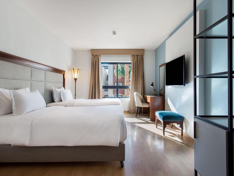 Moderne hotelkamer met groot bed, houten vloer en raam met gordijnen.