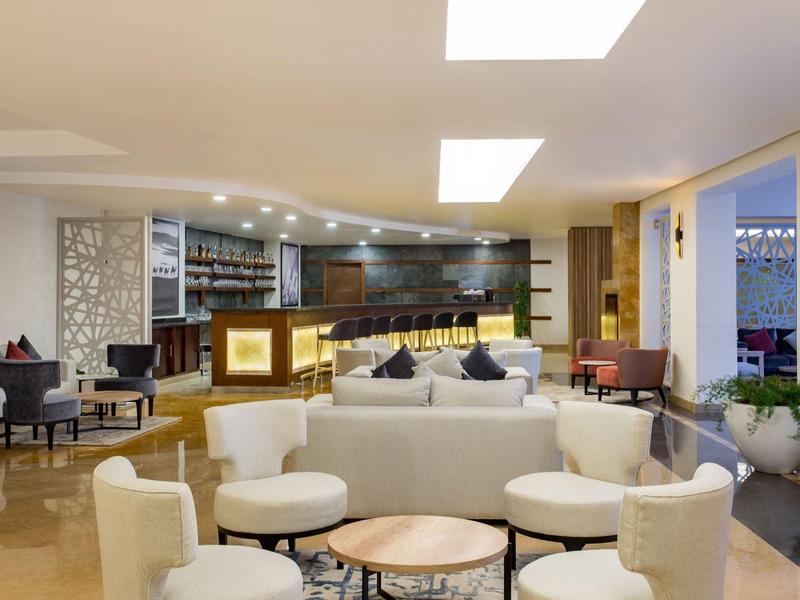 Moderne hotellobby met banken, fauteuils en een verlichte bar op de achtergrond.