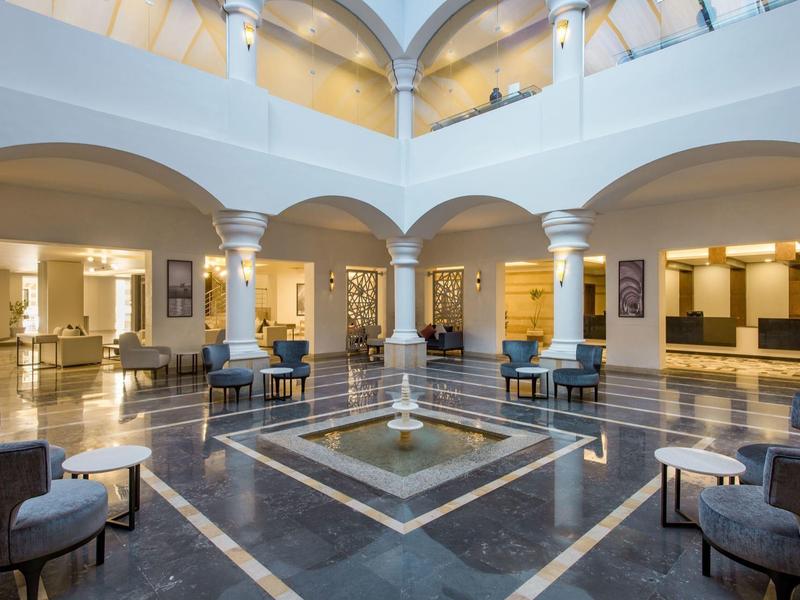 Ruime hotellobby met marmeren vloer, elegante stoelen en hoog plafond met bogen.