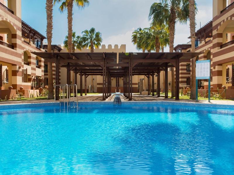 Blauw zwembad voor een hotel met palmbomen en parasols