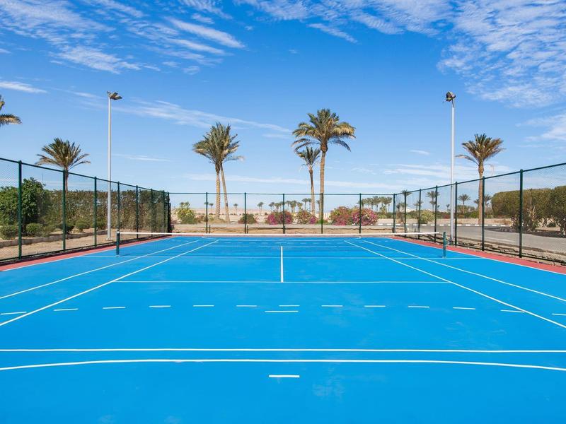 Buiten blauwe tennisbaan met palmbomen onder een blauwe lucht.