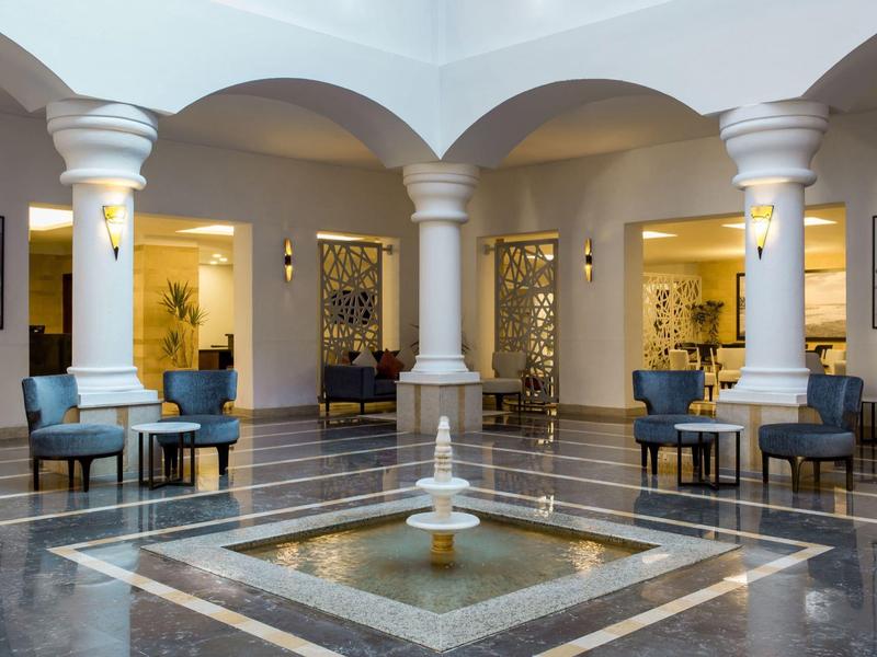 Elegante hotel lobby met zitgedeelte en centrale fontein onder zuilenbogen.