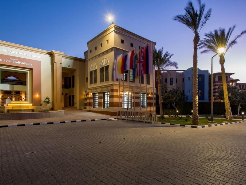 Hotelgebouw bij schemering met verlichte ramen en palmbomen op de voorgrond.