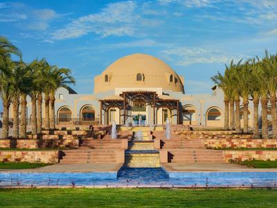 Hotel elegante con viale di palme e fontana centrale davanti a struttura a cupola.