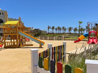 Area giochi colorata con scivoli e struttura per arrampicata davanti a un hotel e palme.