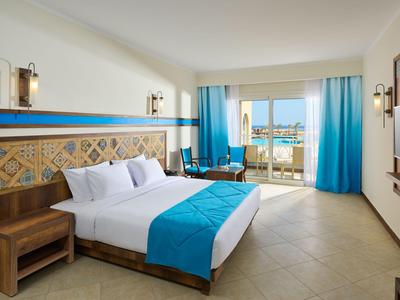 Camera d'hotel luminosa con letto matrimoniale, accenti blu e balcone con vista mare.