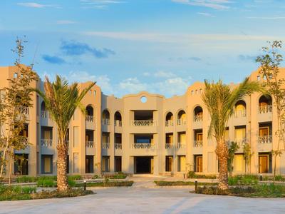 Complesso alberghiero moderno con tre piani, archi e palme sotto un cielo limpido.