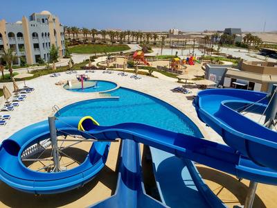 Ampia area piscina con scivoli d'acqua e lettini in un resort estivo soleggiato.