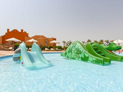 Wasserpark mit grünen und blauen Wasserrutschen in einem flachen Pool bei sonnigem Wetter.