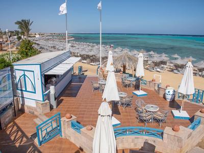 Terrasse mit weißen Sonnenschirmen und blauen Sitzkissen am Meer bei klarem Himmel