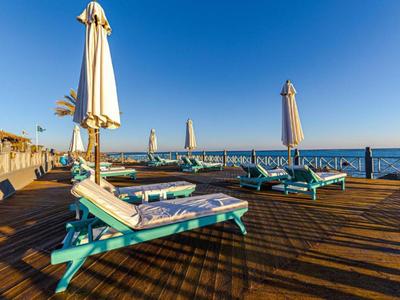Liegestühle mit Handtüchern auf einem Holzsteg am Meer unter blauem Himmel.
