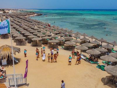 Strand mit vielen Sonnenschirmen, Menschen und klarem blauem Wasser neben Hotelanlagen.